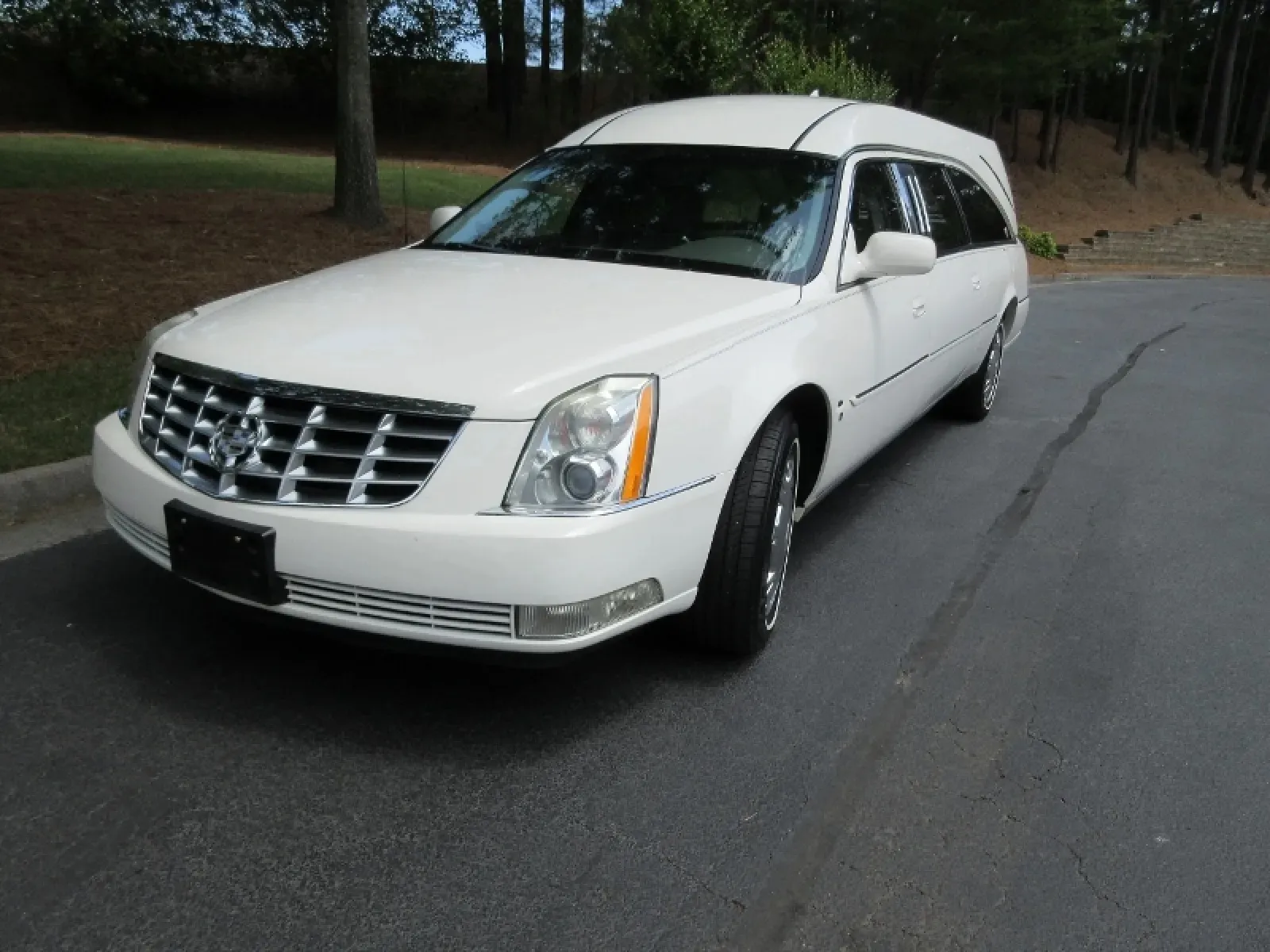 Luxury white Cadillac hearse parked on a road surrounded by trees.
