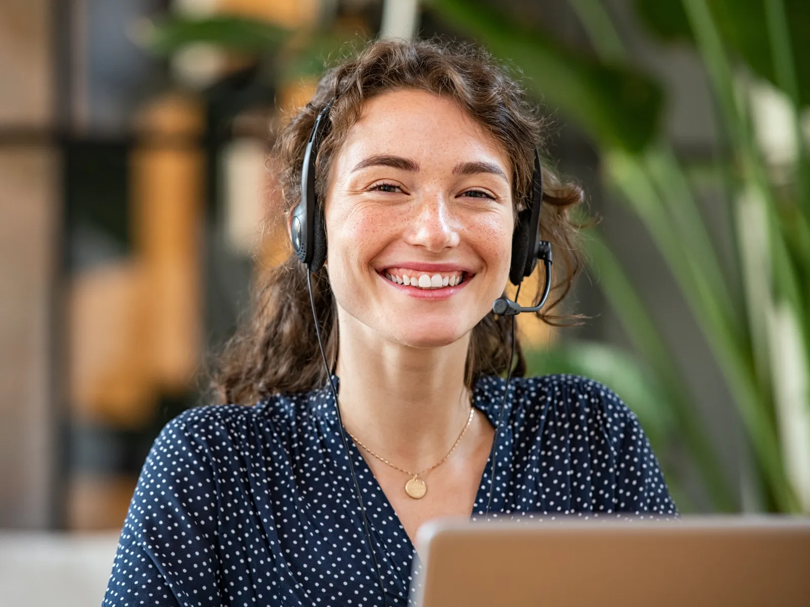 Smiling woman wearing headset working on a laptop in a bright modern office environment.