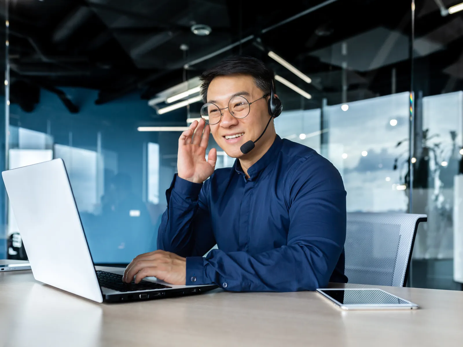 Two customer service representatives wearing headsets working on computers in a modern office with large windows.