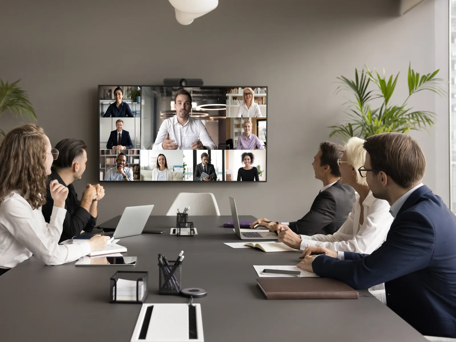 Business team in office conference room participating in a video meeting with remote colleagues on a large screen.