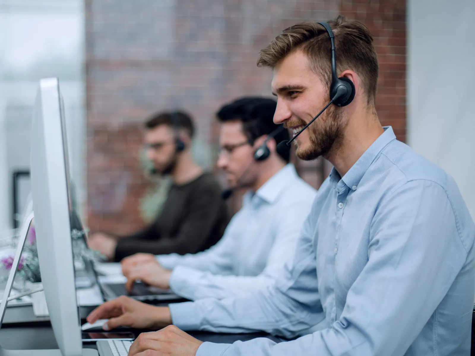 Customer service representatives wearing headsets working at computers in a modern office.
