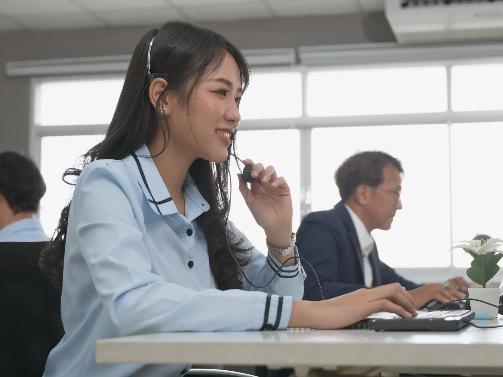 Customer service representative wearing headset and typing on keyboard in busy office environment