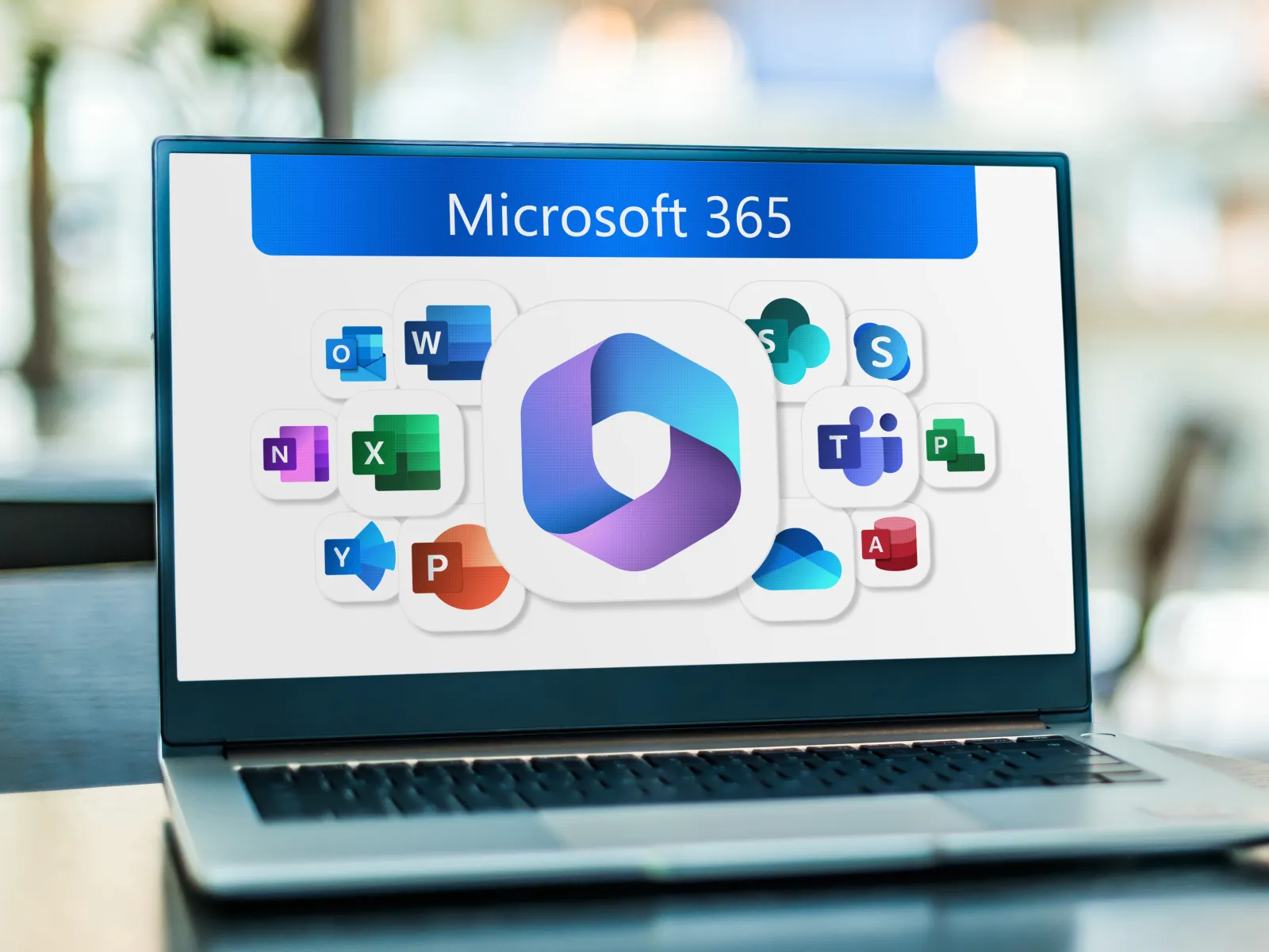 Laptop displaying Microsoft 365 apps icons on screen with blurred office background.