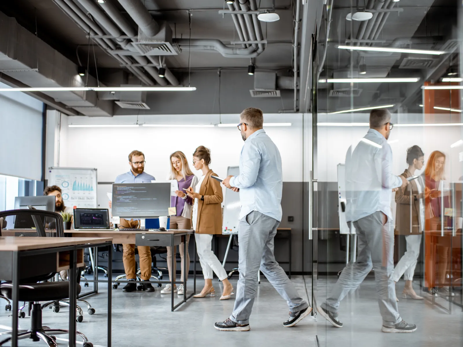 Team of professionals collaborating in a modern office with glass walls and computers during a meeting.