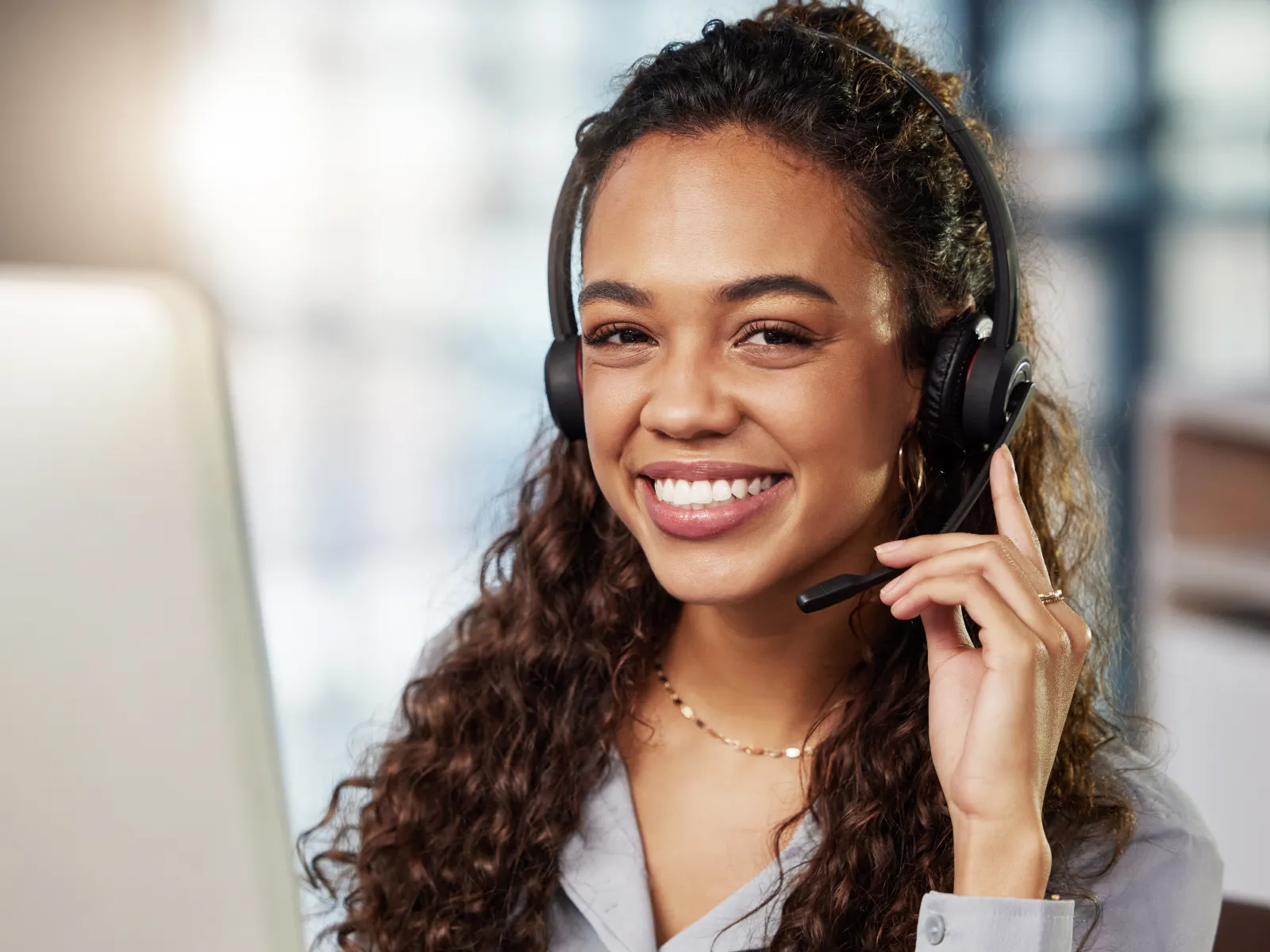 Smiling customer support representative with curly hair wearing a headset in an office setting