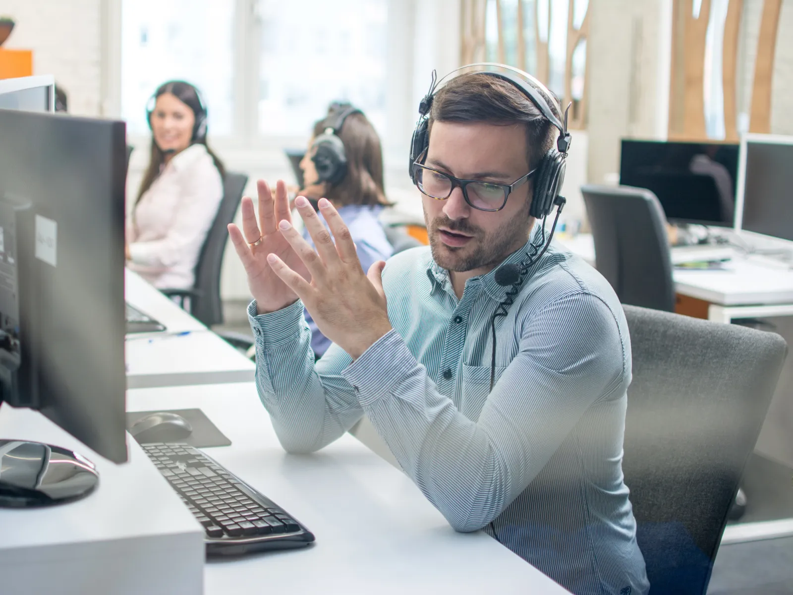 Man wearing headset explaining something at a computer desk in a modern office environment