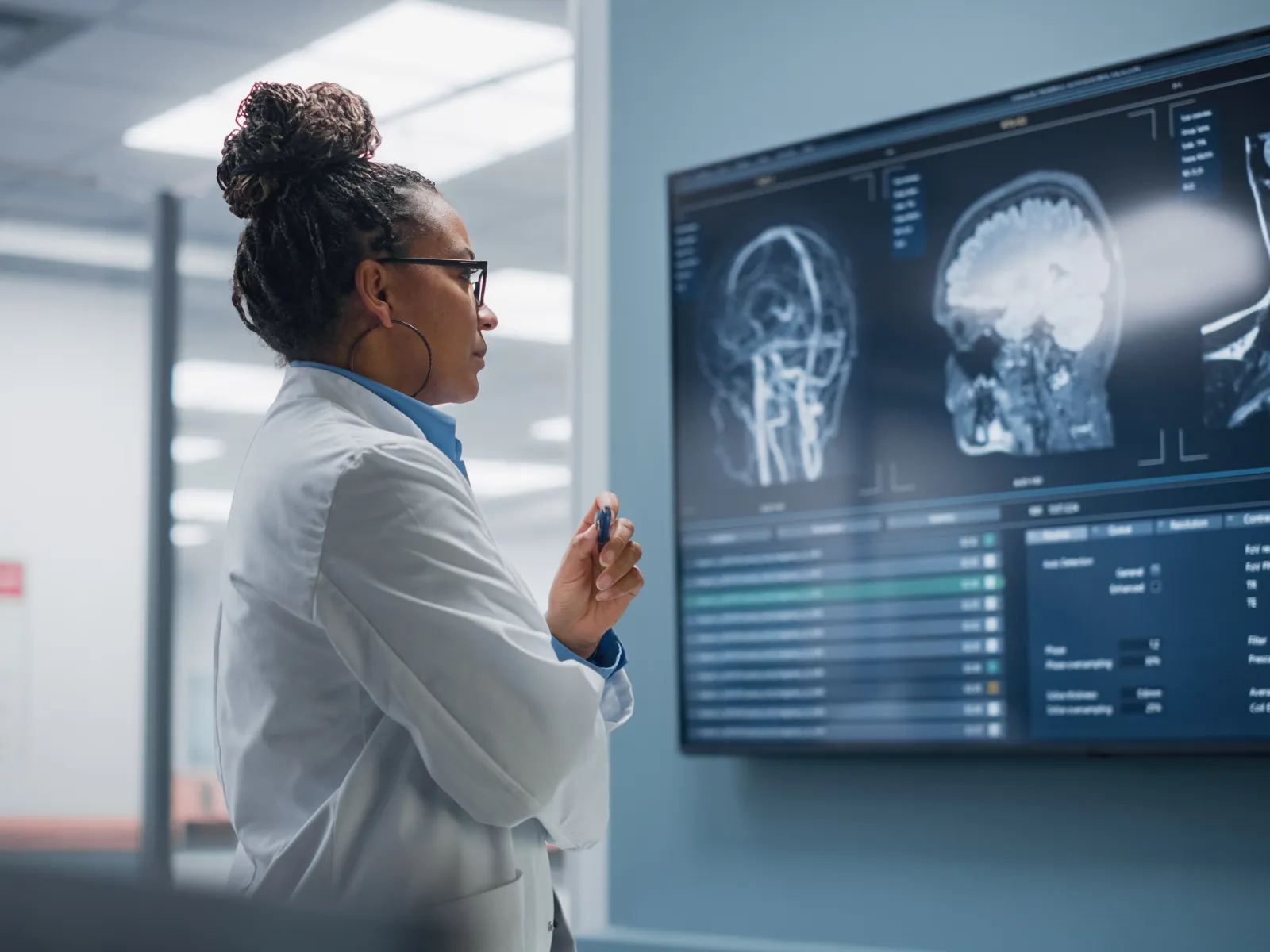 Female doctor examines brain MRI scans on a large monitor in a modern hospital setting.