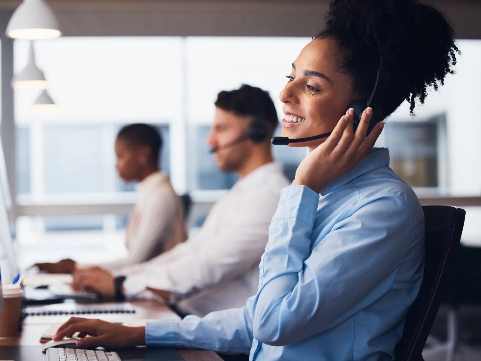Customer service team working with headsets in modern office environment, smiling and assisting clients.