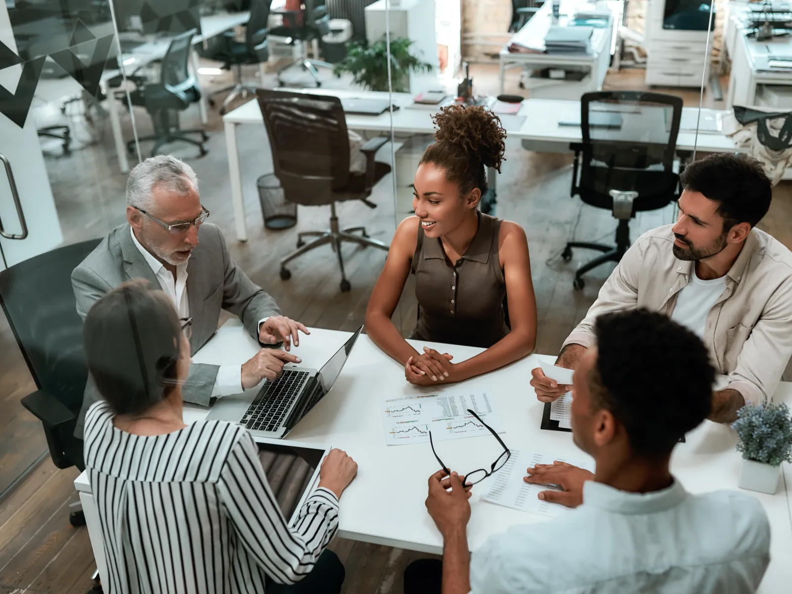 Diverse team discussing business charts and data around a white office table in a modern workspace.