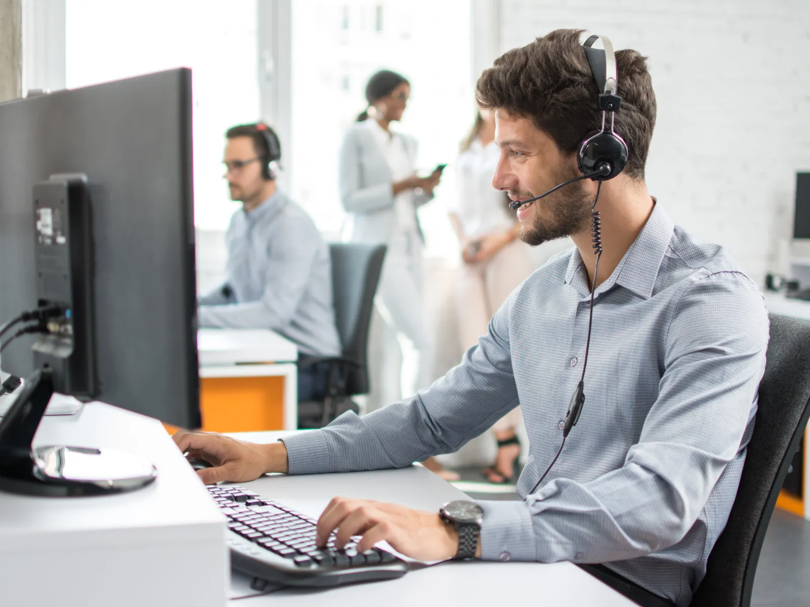 Customer service representative wearing headset working on computer in modern office with colleagues