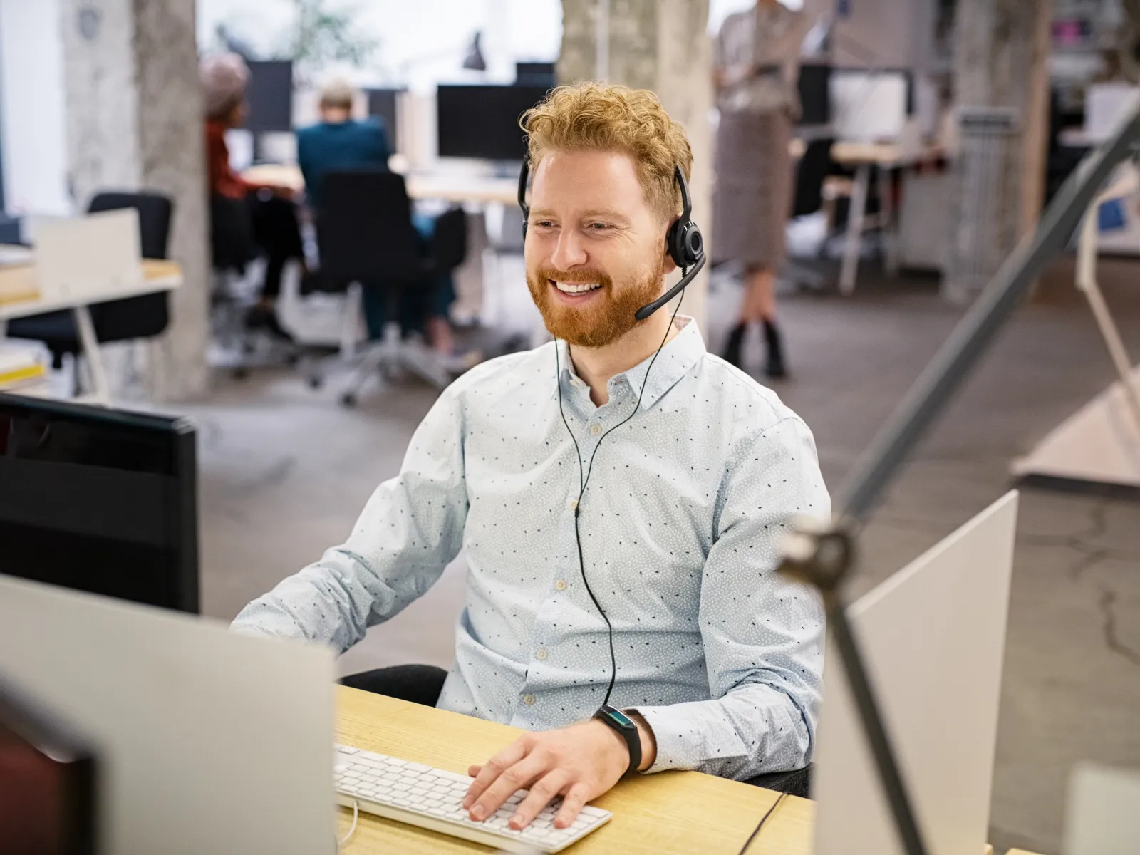 Smiling customer service representative wearing headset and working at computer in modern office environment