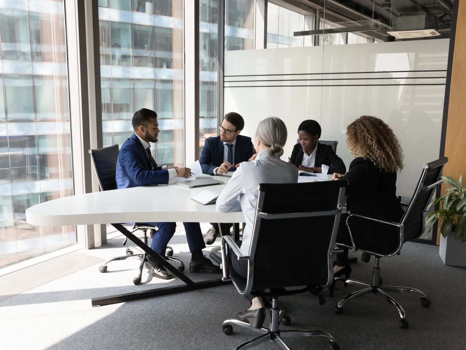 Diverse business team in formal attire having a meeting around a white conference table in a modern office.