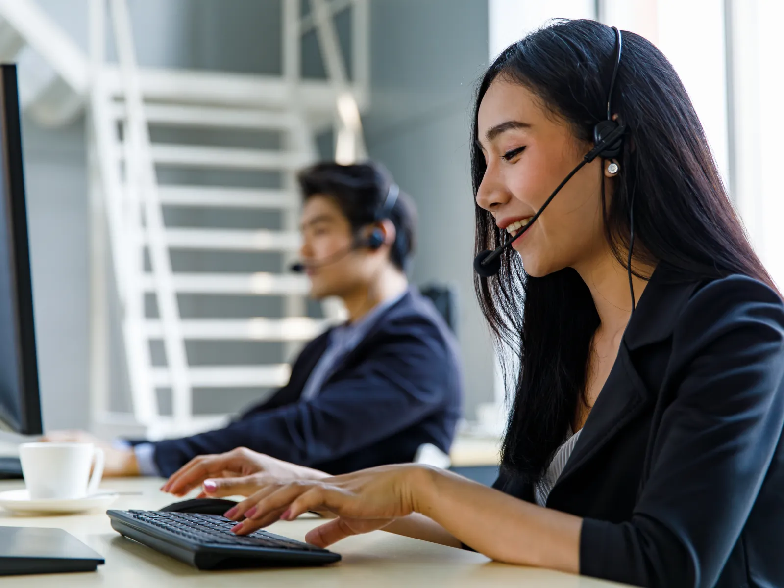 Two customer service representatives wearing headsets working at computers in a modern office environment