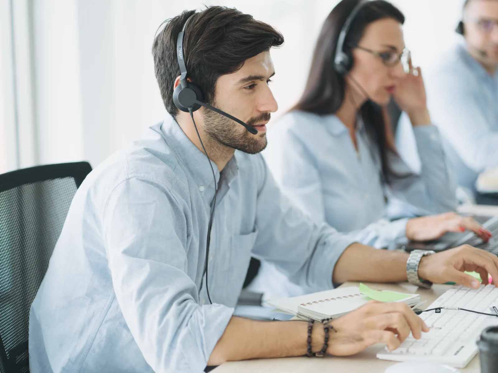Customer service team working with headsets in modern office environment, smiling and assisting clients.