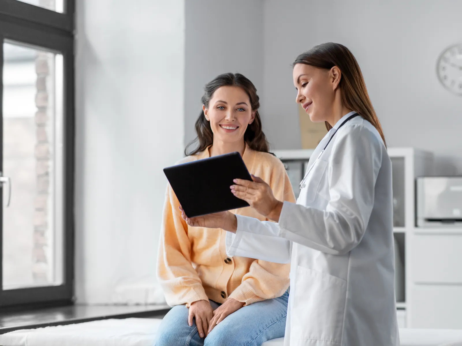 Doctor showing medical information on tablet to female patient during consultation in clinic.