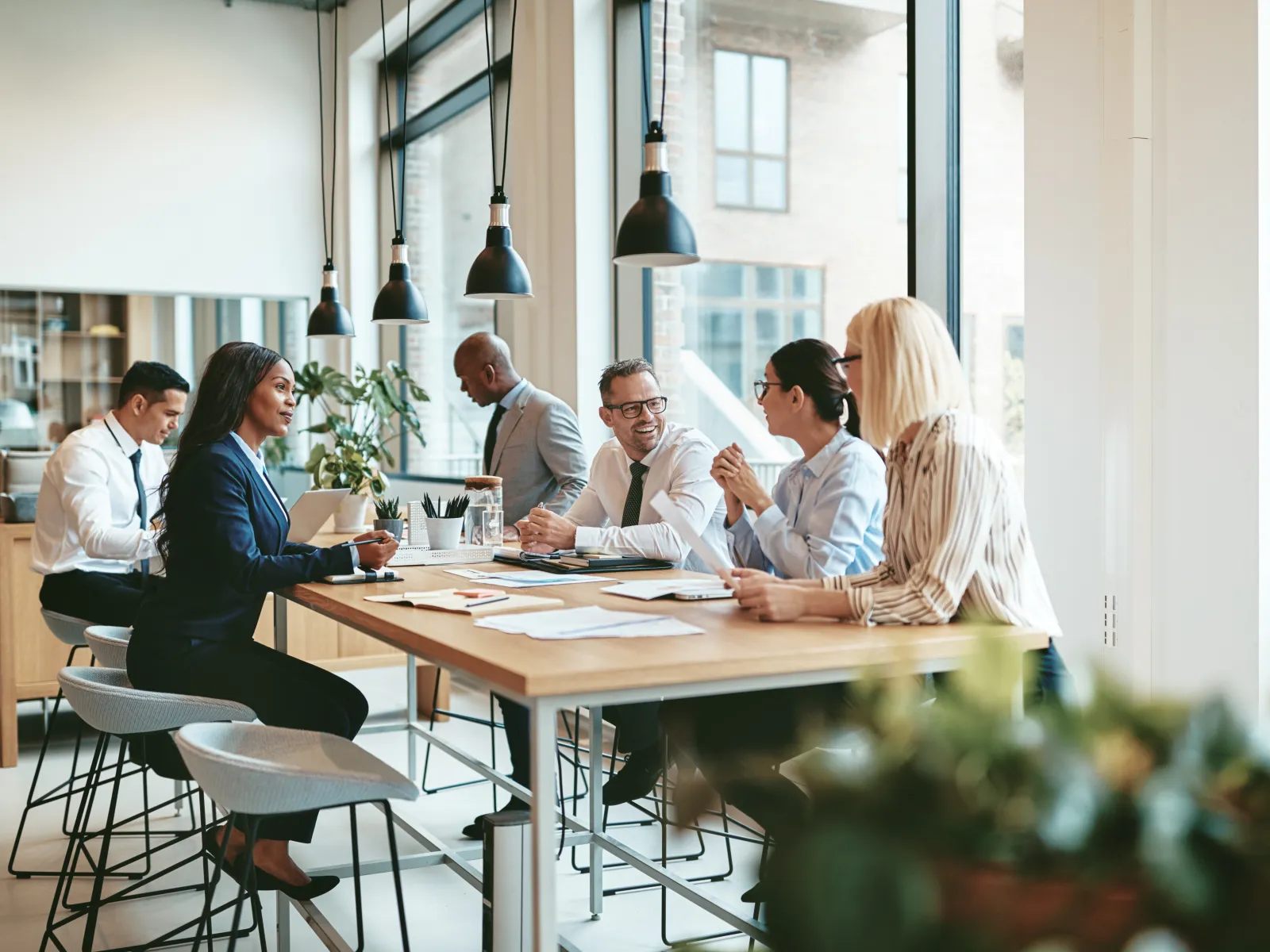 Diverse business team engaged in a meeting around a table in a modern office with large windows and natural light
