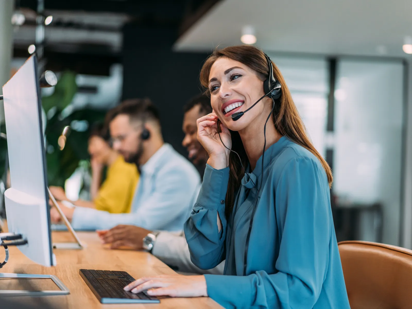 Smiling customer service representative wearing headset working at computer in a modern call center office