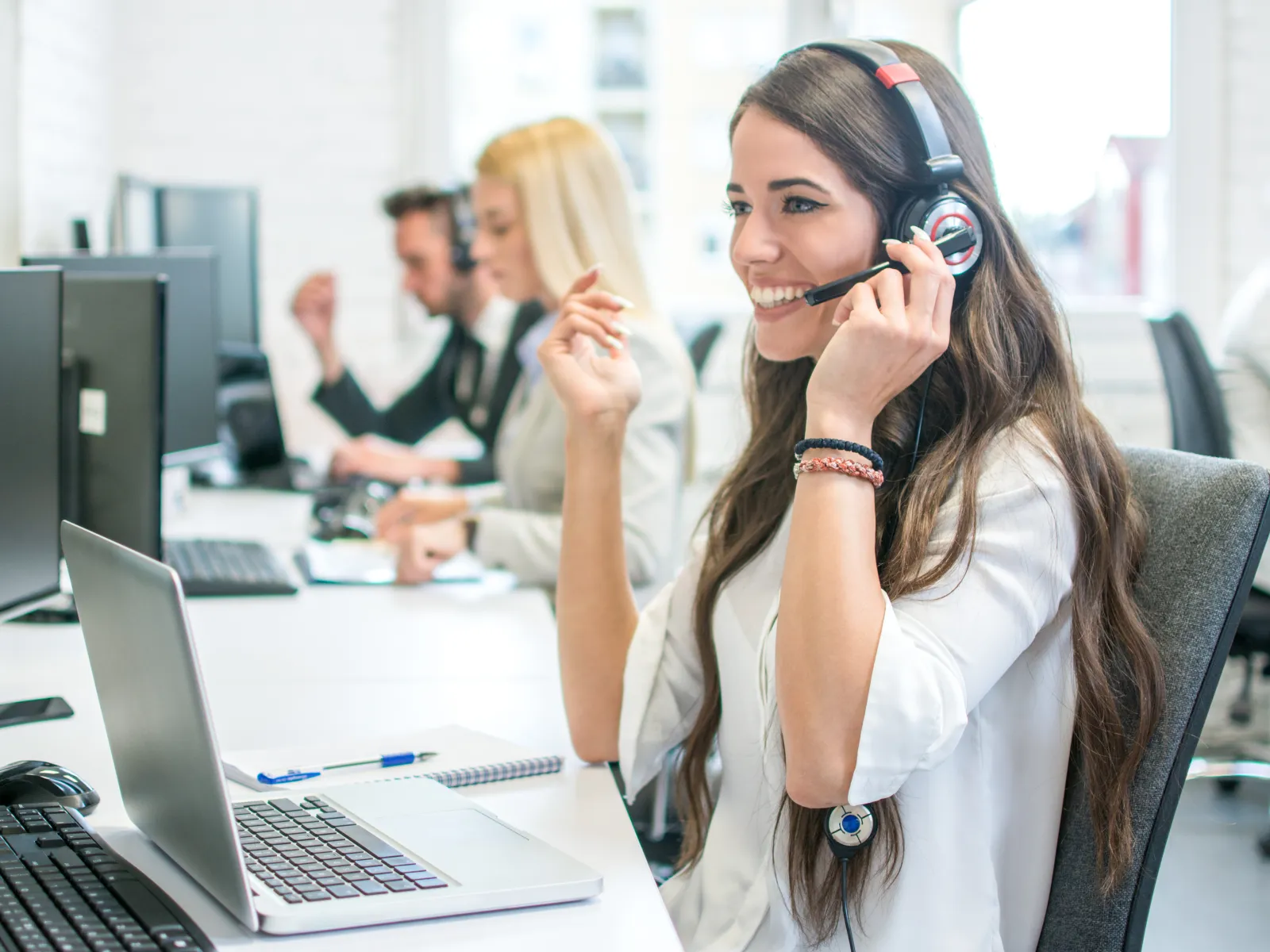 Smiling female customer service agent with headset working on laptop in a modern office environment