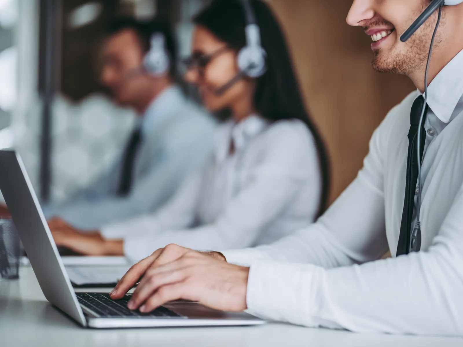 Customer service representatives wearing headsets working on laptops in a modern office environment.