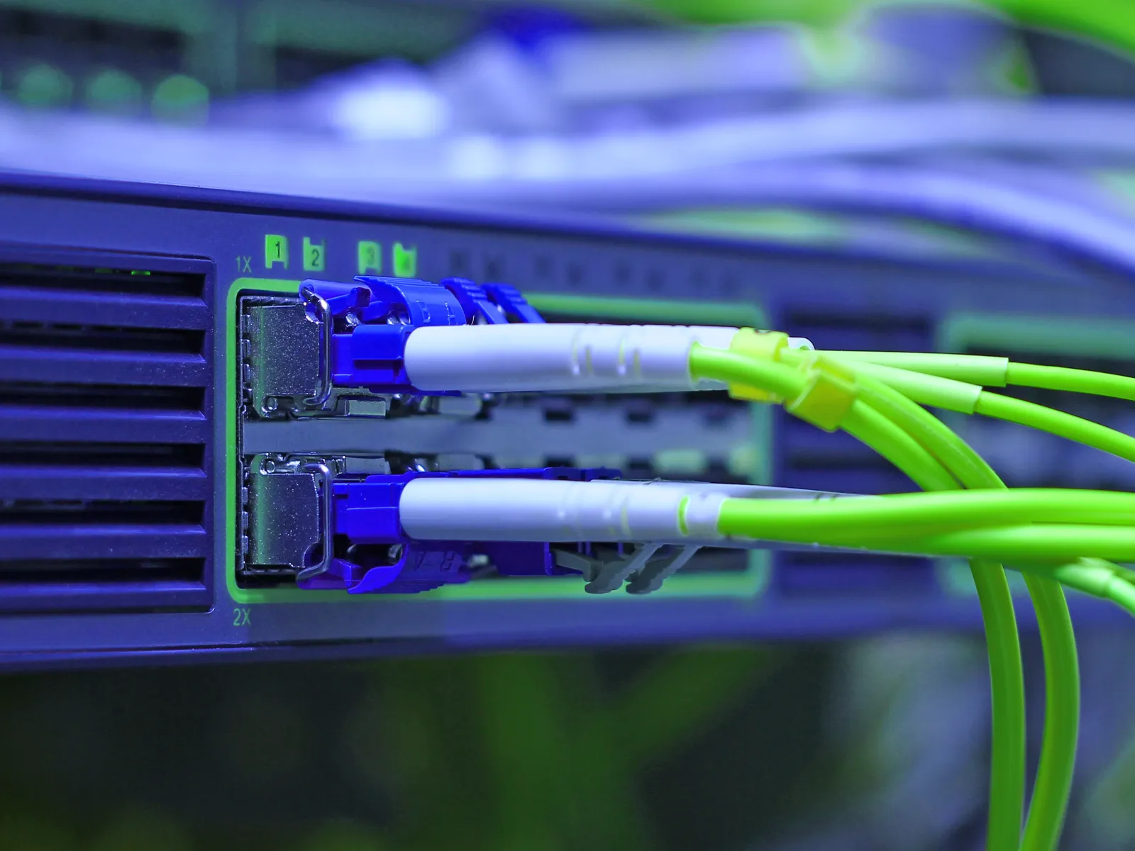 Close-up of green fiber optic cables connected to a network switch in a data center setup.