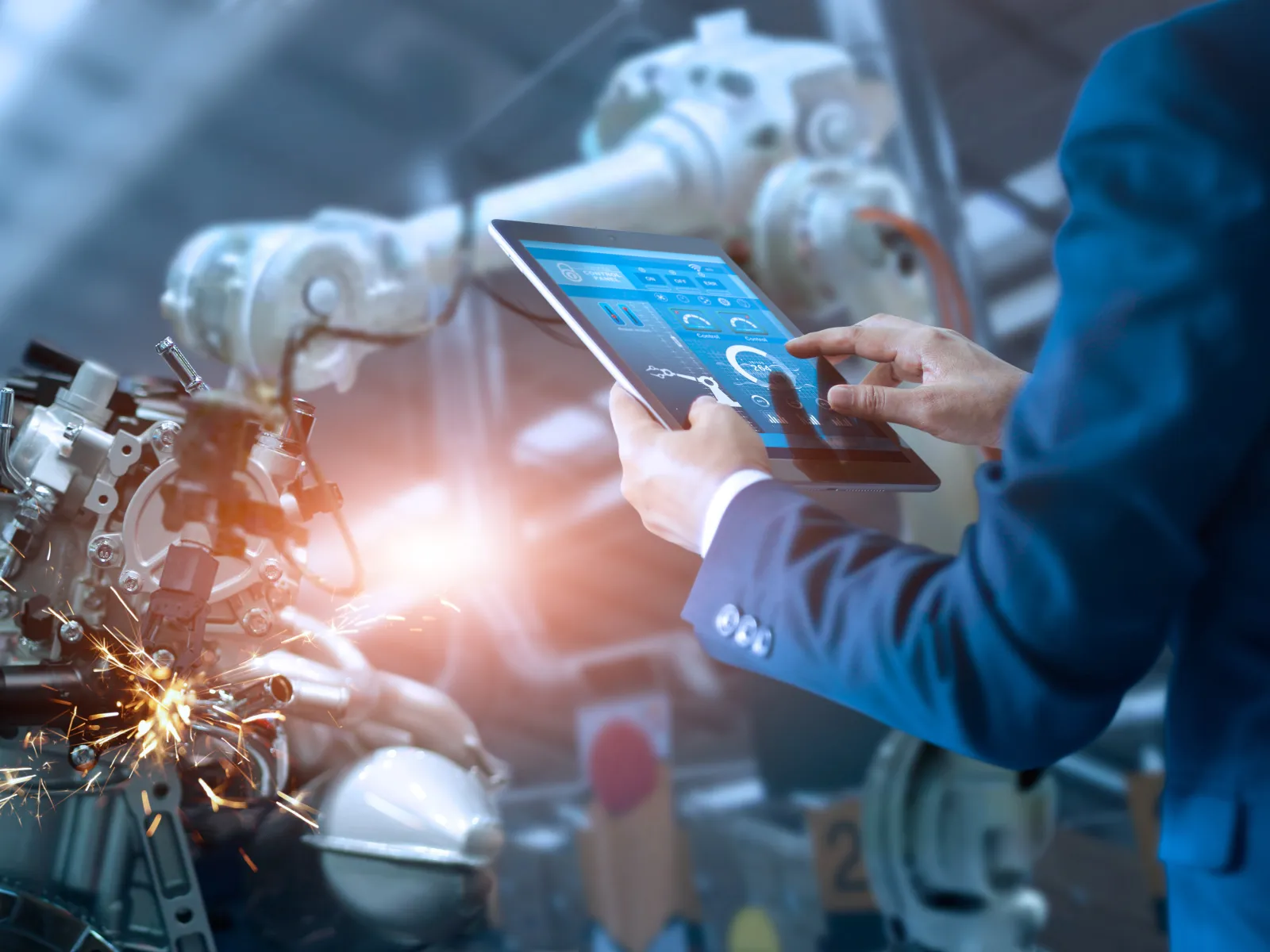 Engineer controls robotic machinery with tablet for automated manufacturing and precision welding in factory setting