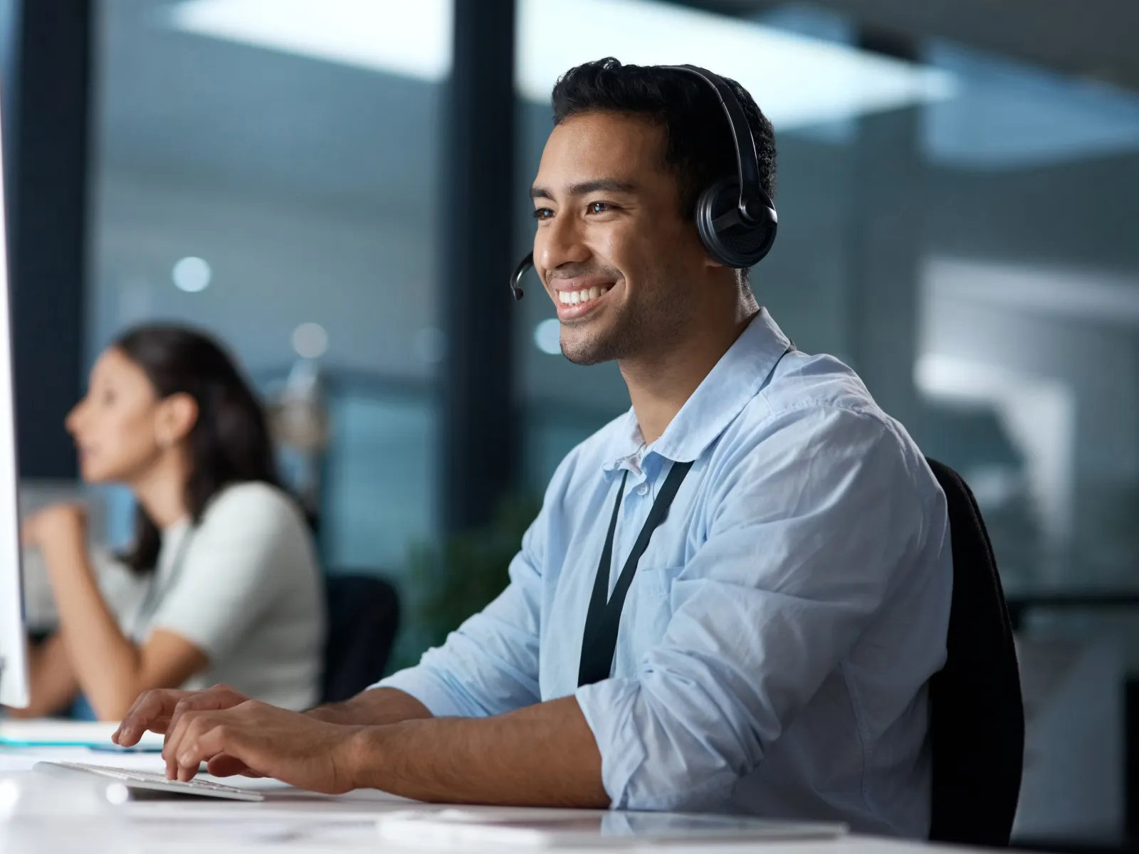 Smiling male customer service agent wearing headset working at computer in modern office environment