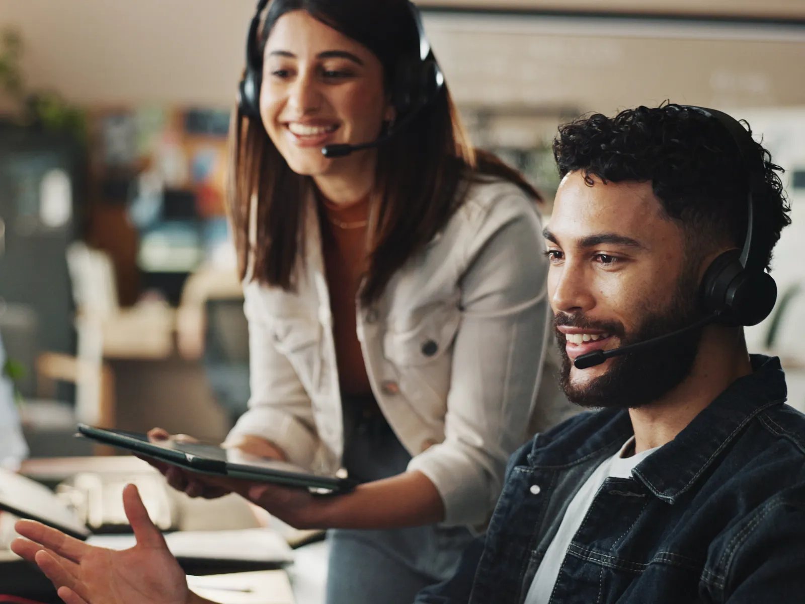 Two diverse customer service agents with headsets collaborating and smiling in a modern office environment.