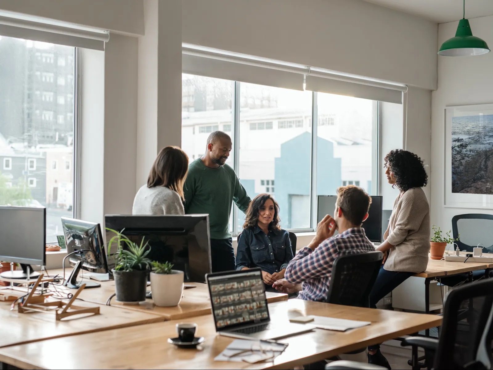 Group of diverse colleagues collaborating in a modern office with large windows and plants.