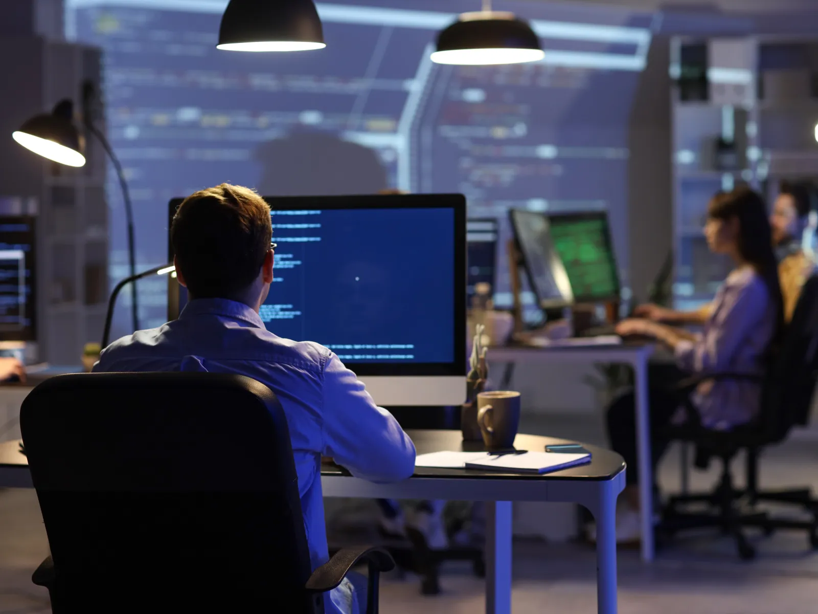Software developers working late in office with multiple computer screens displaying code.