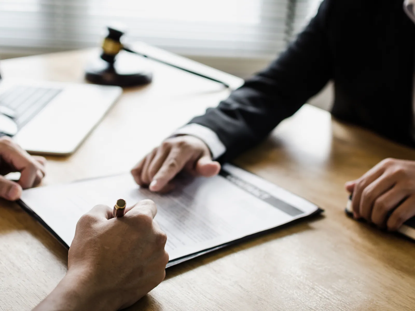 Close-up of two people discussing and signing a legal document at a wooden desk with a gavel and laptop nearby
