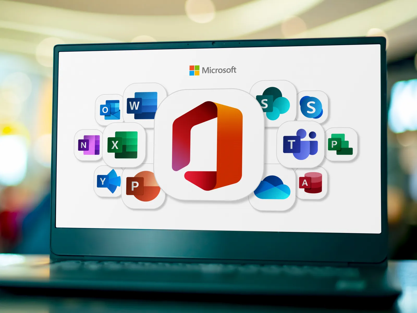 Laptop screen displaying Microsoft Office suite icons against a blurred indoor background.