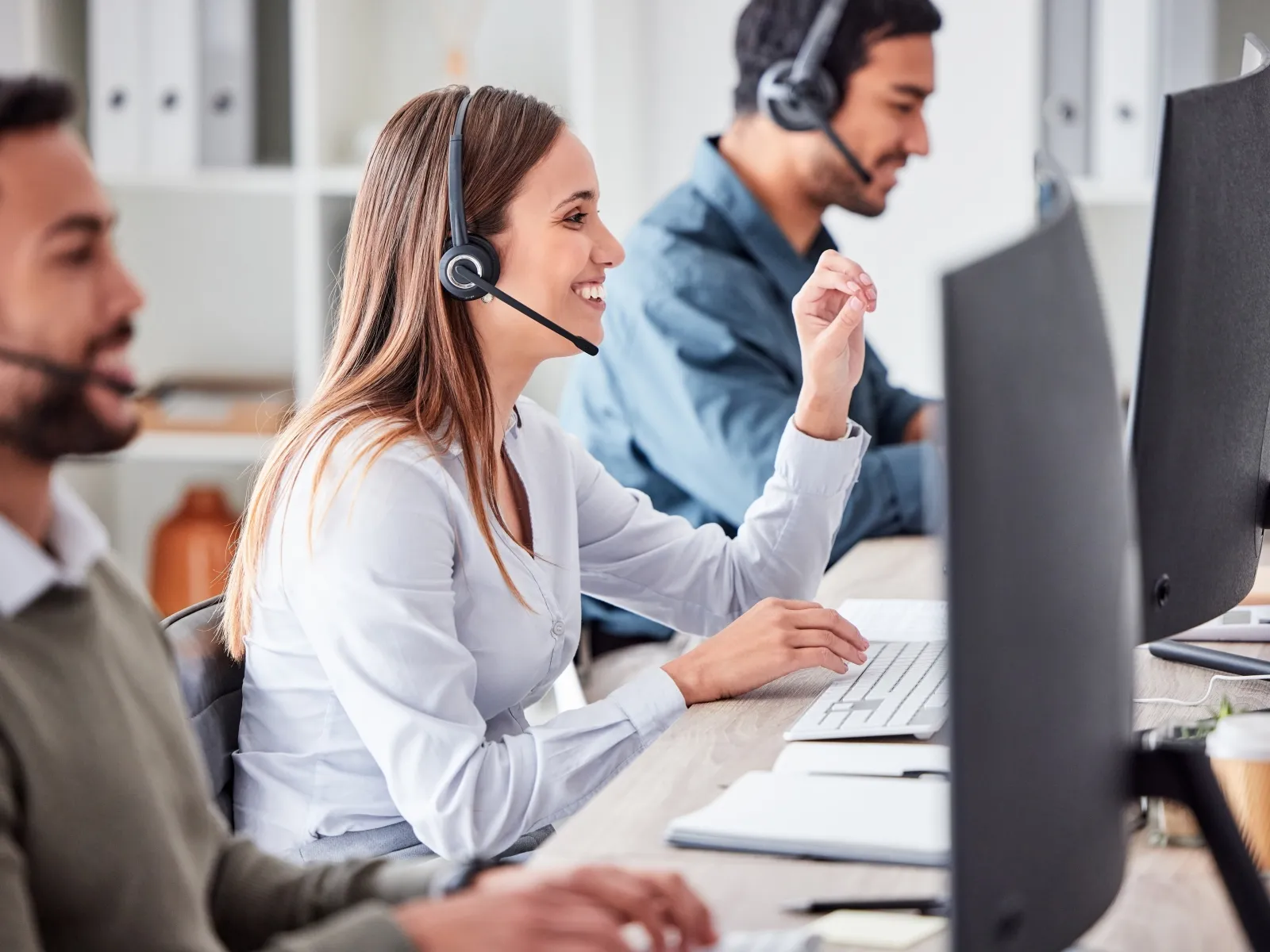 Customer service team wearing headsets working at desks with computers in a modern office environment.