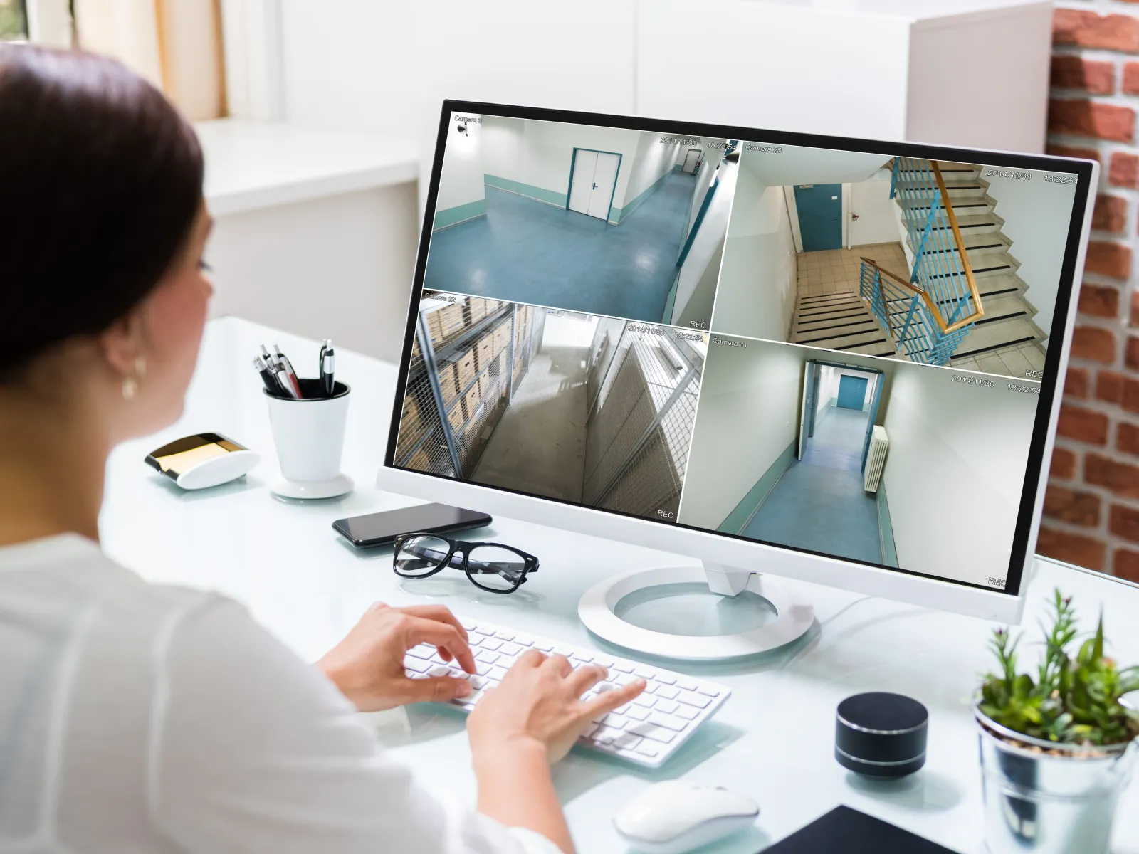 Woman monitoring security camera footage of hallways and staircases on a computer screen at a desk.