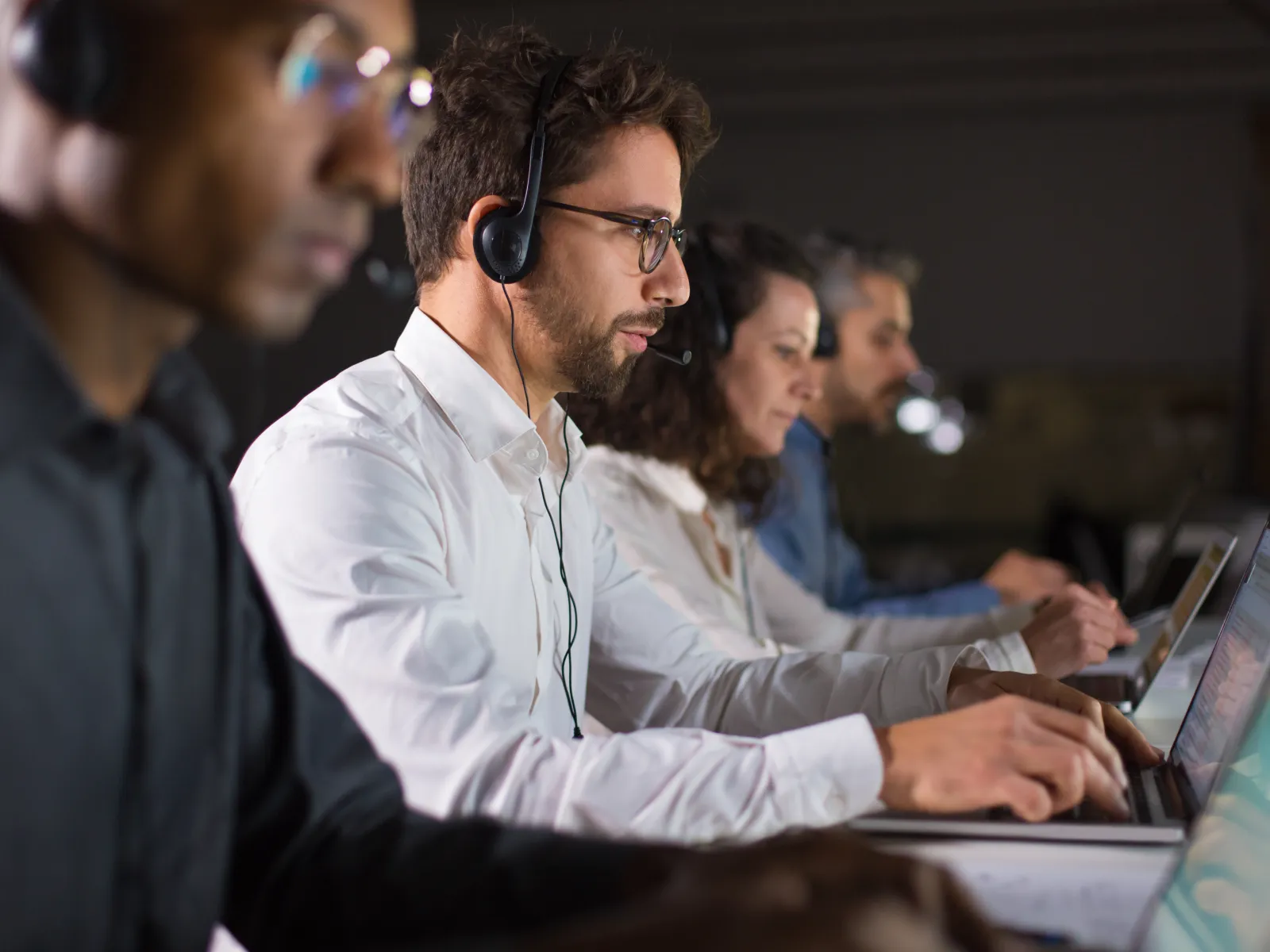 Customer service team wearing headsets working on laptops in a call center environment.