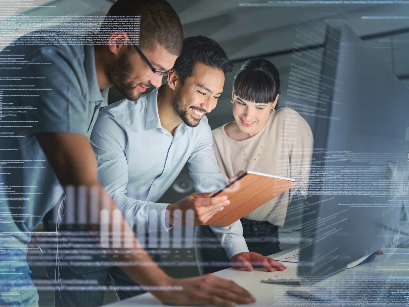 Three young professionals collaborating over a tablet and computer with code overlays in a modern office setting
