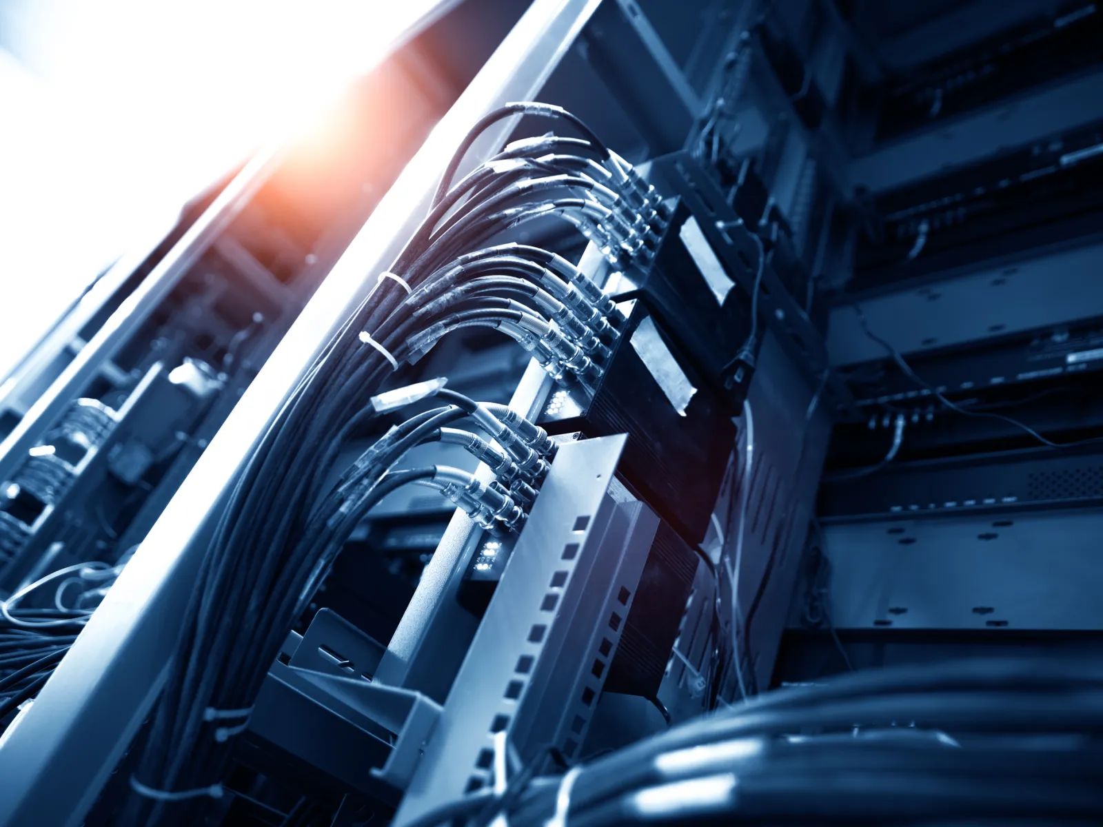 Close-up of network cables and hardware connections inside a data center rack with blue lighting.