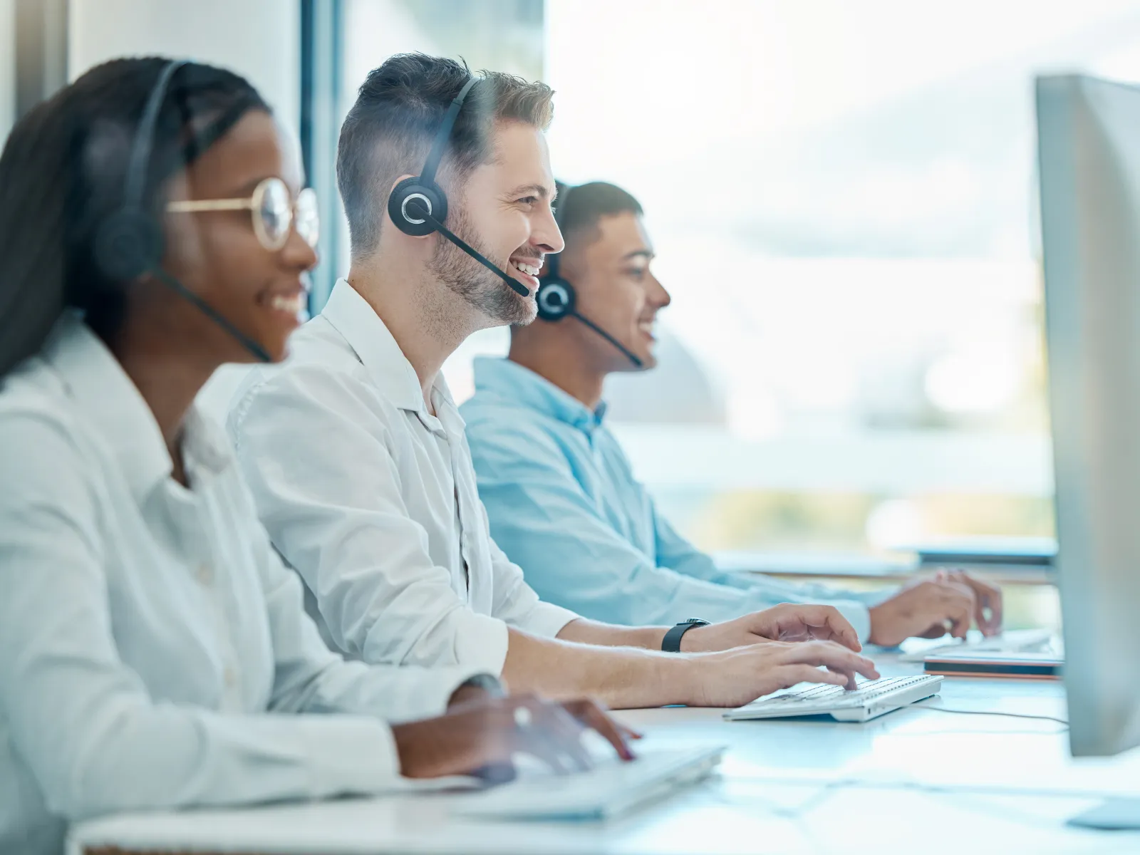 Customer service team wearing headsets working on laptops in a call center environment.