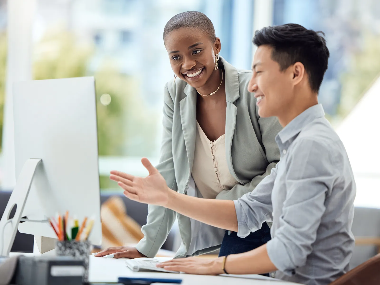 Two colleagues smiling and discussing work at a computer in a modern office setting