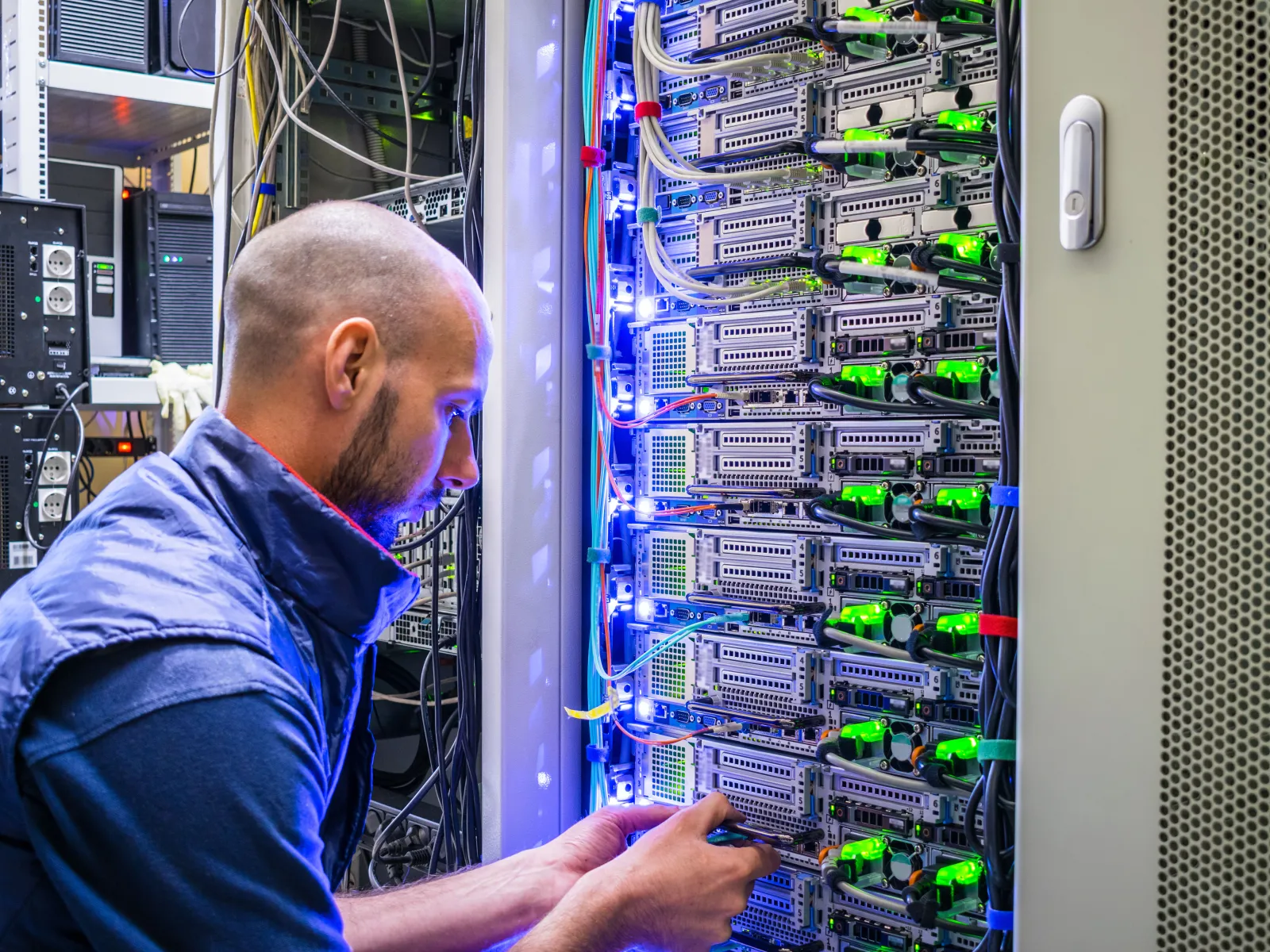 Technician working on a server rack with glowing LEDs and network cables in a data center.