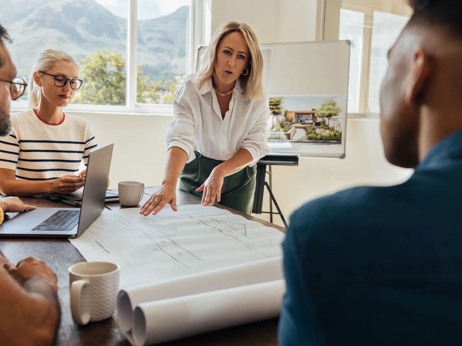 Architect discussing building plans with colleagues around a table in a bright modern office with mountain views.