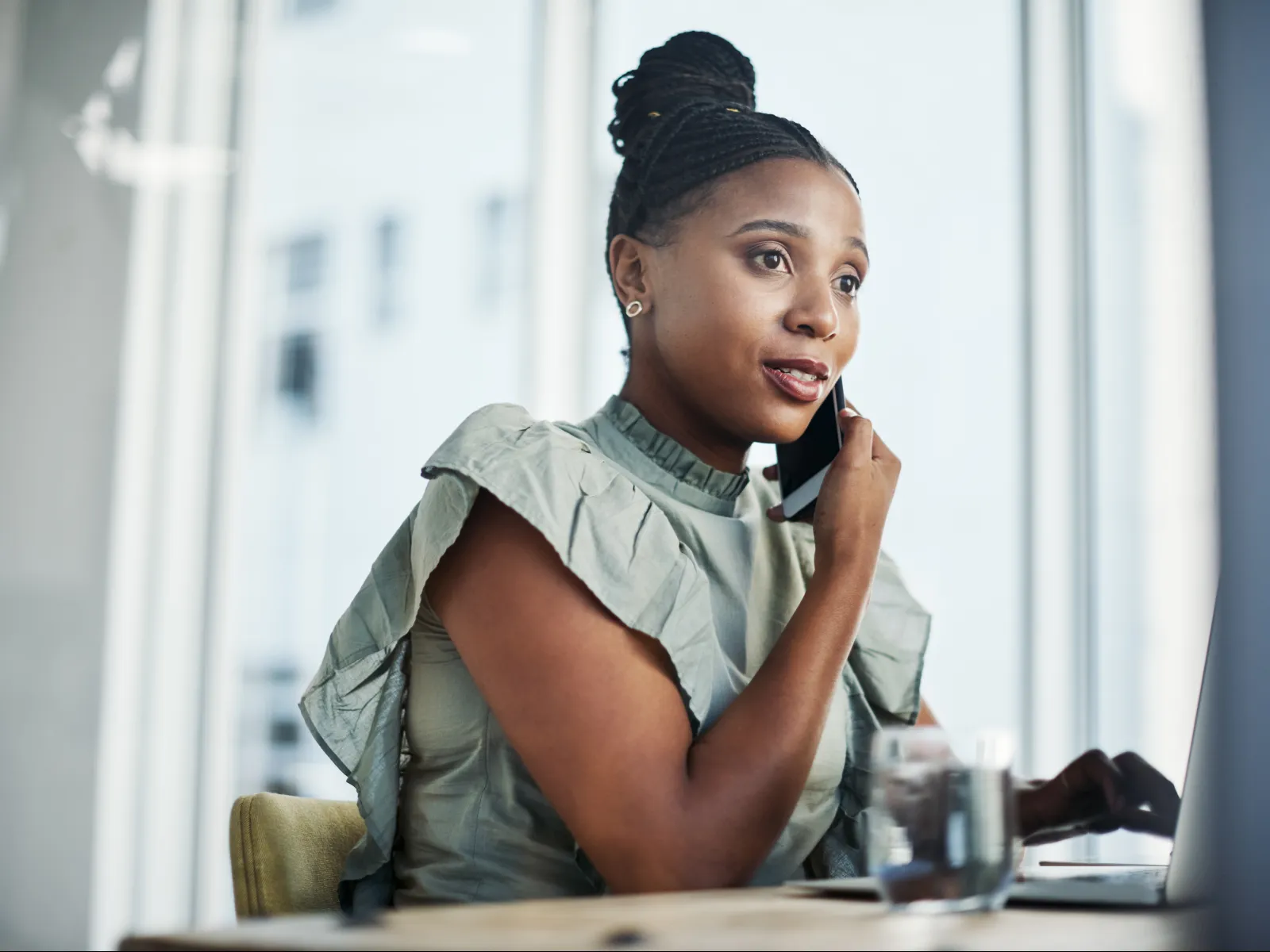 Confident woman on phone at desk with laptop and water glass, focused on conversation.