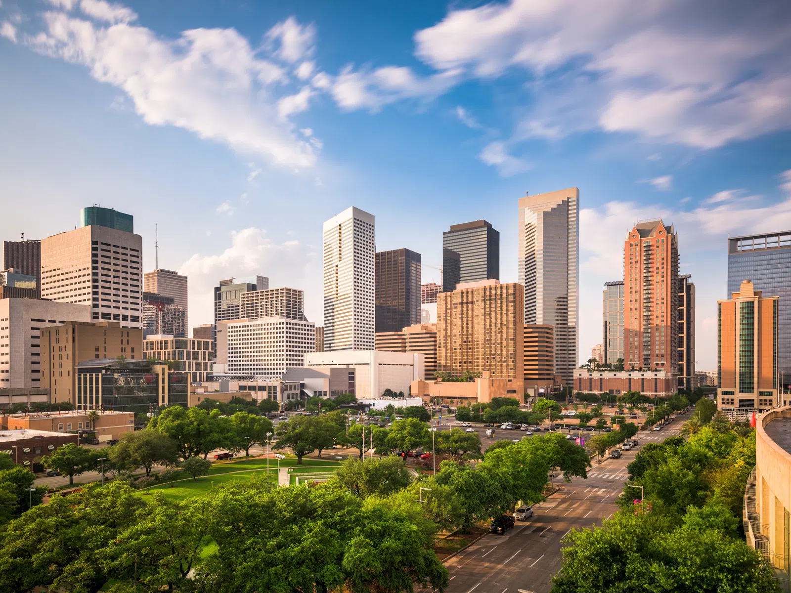 Houston city skyline with tall buildings, green park, and blue sky with scattered clouds on a sunny day