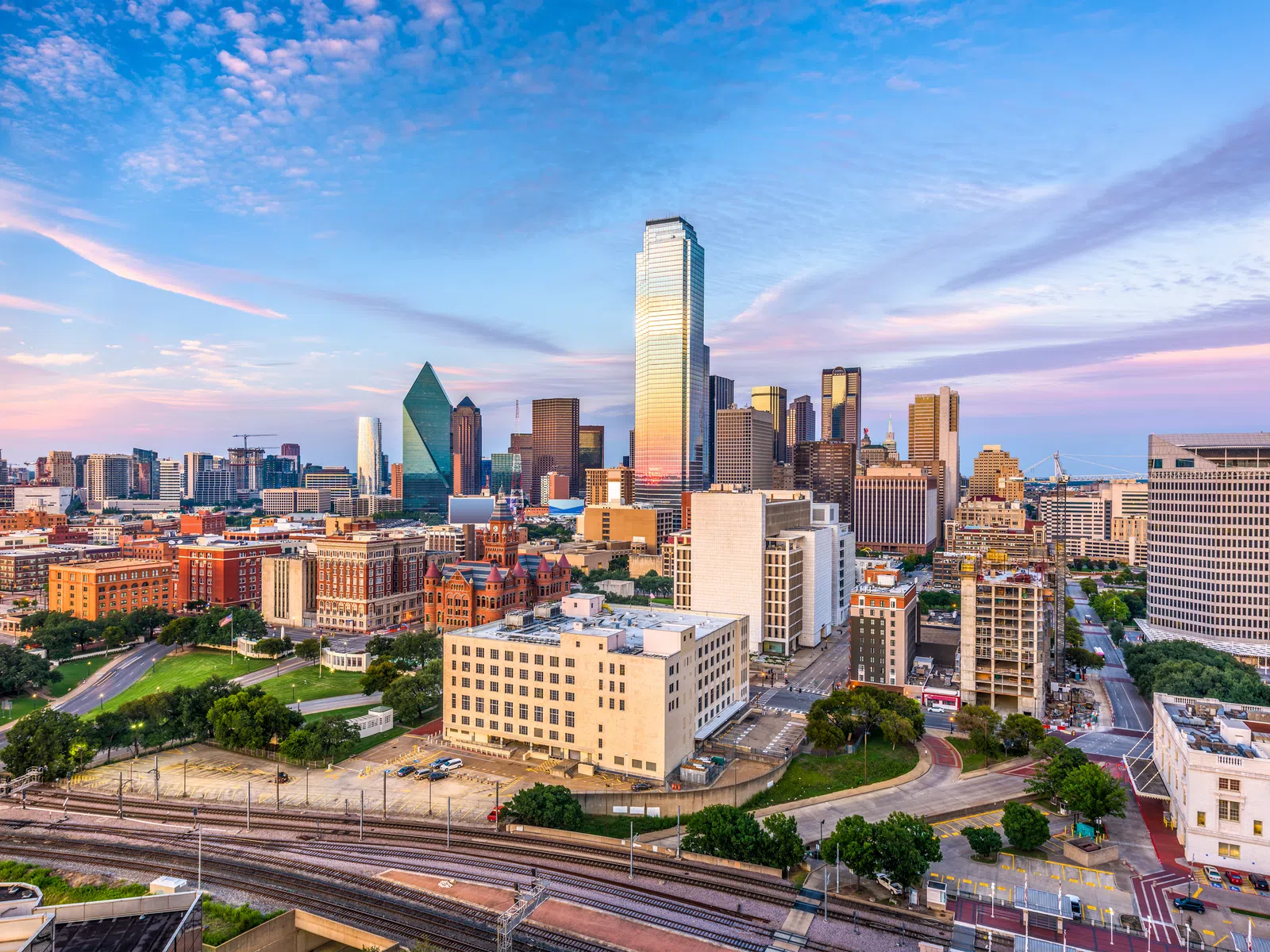 Dallas skyline at sunset with iconic buildings and colorful sky over the cityscape.