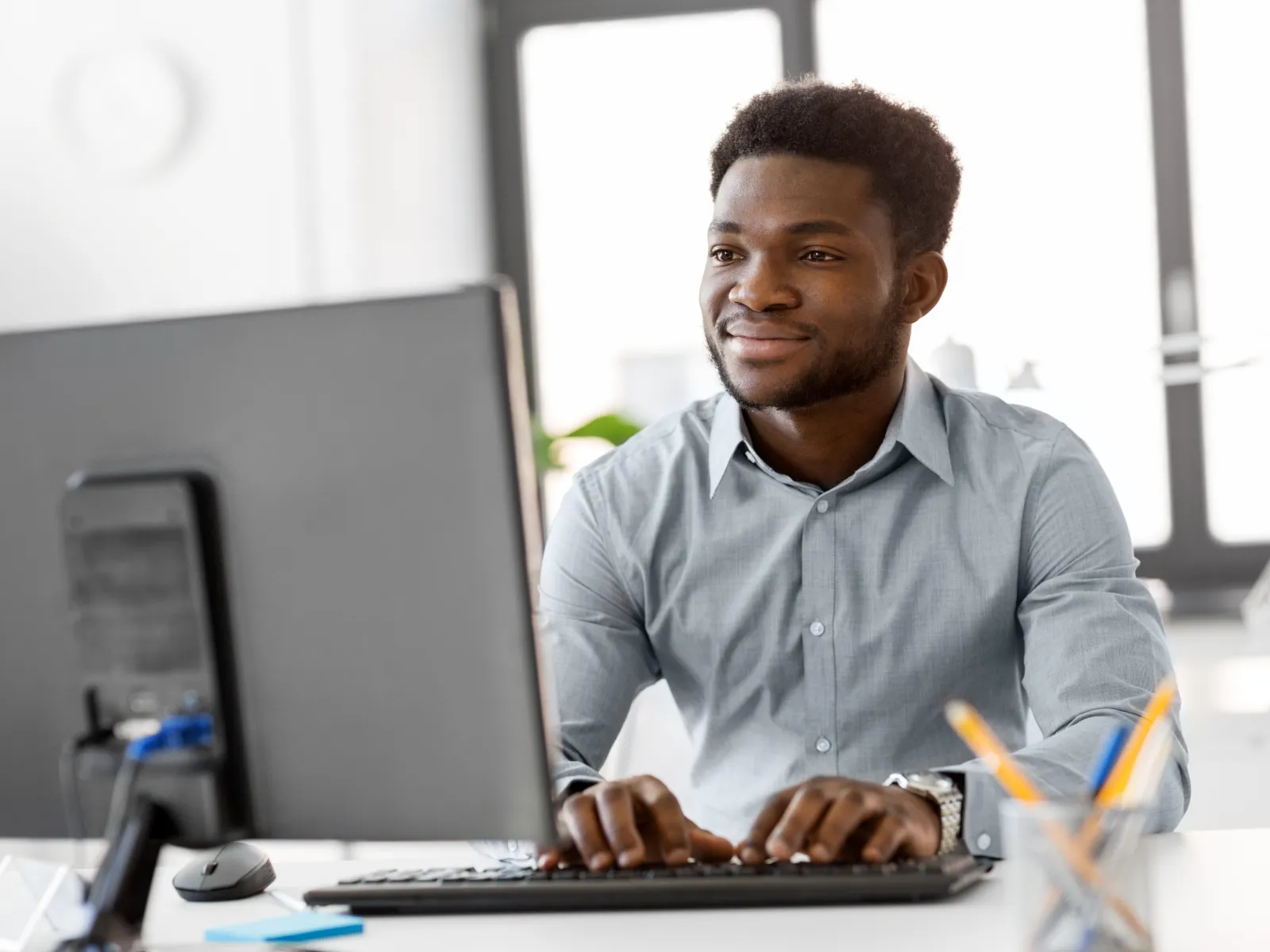 Smiling man working on a computer at a modern office desk with stationery.