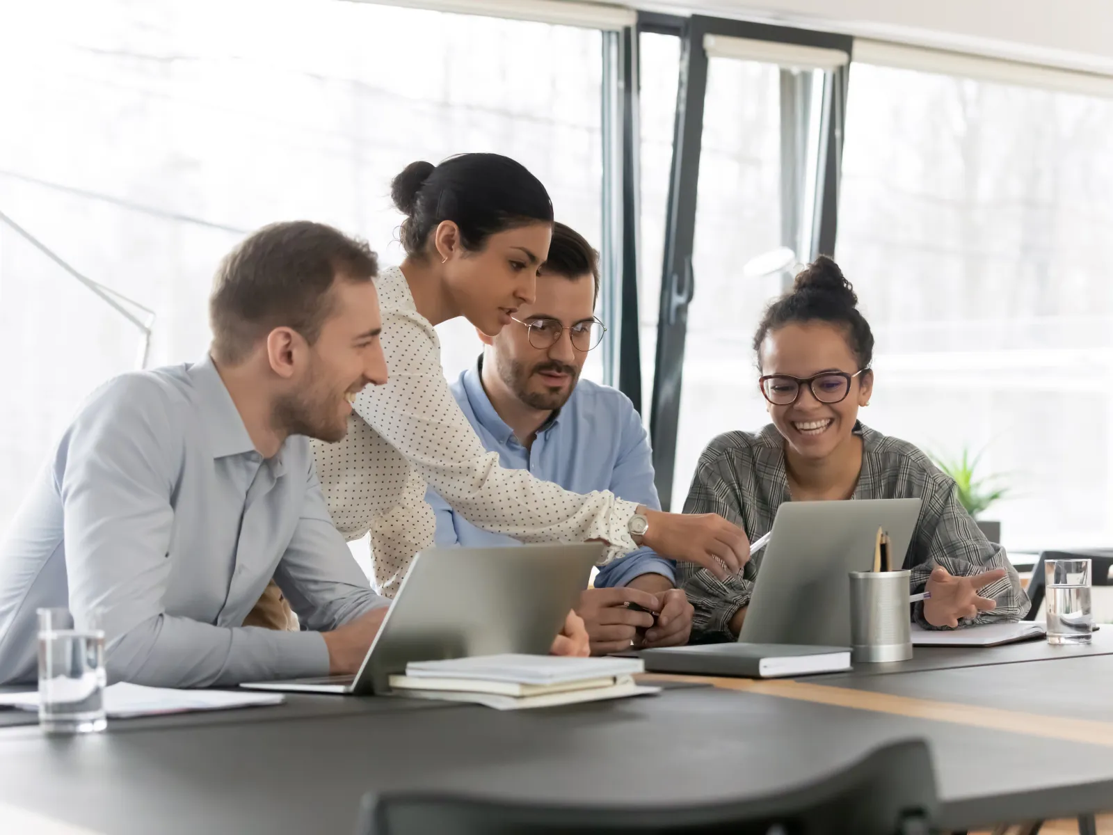Professionals collaborating in a modern office, focused on laptops and discussing ideas together.