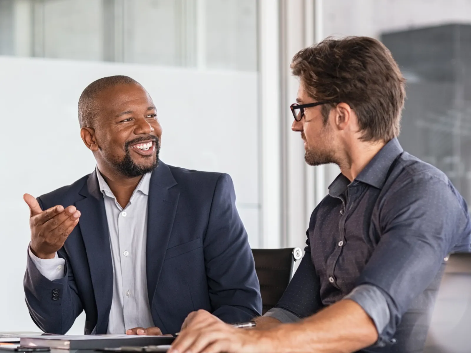 Two men engaged in a business discussion at a conference table in a modern office.