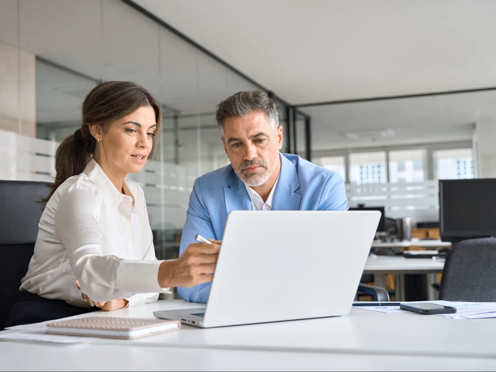 Two professionals discussing a project while looking at a laptop in a modern office.