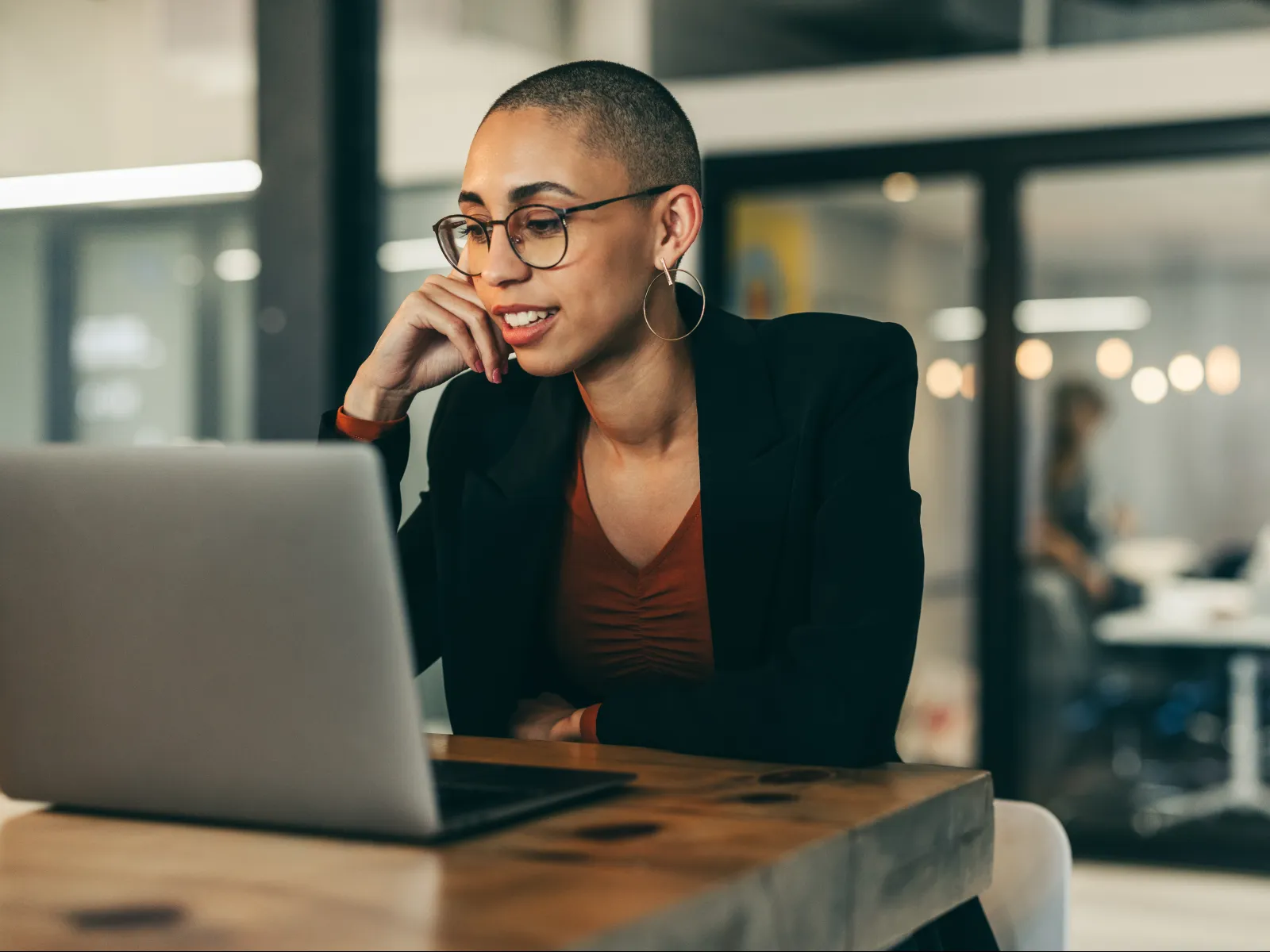 A focused young woman in an office, engaged with her laptop and smiling thoughtfully while on a call.