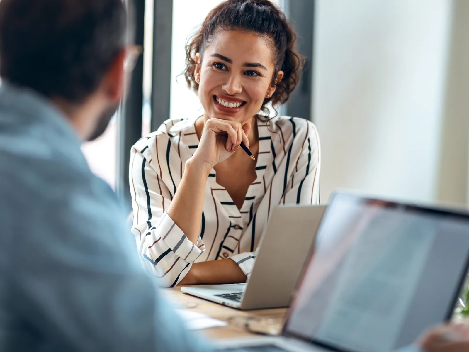 Smiling woman in striped shirt engaging in conversation during a business meeting.