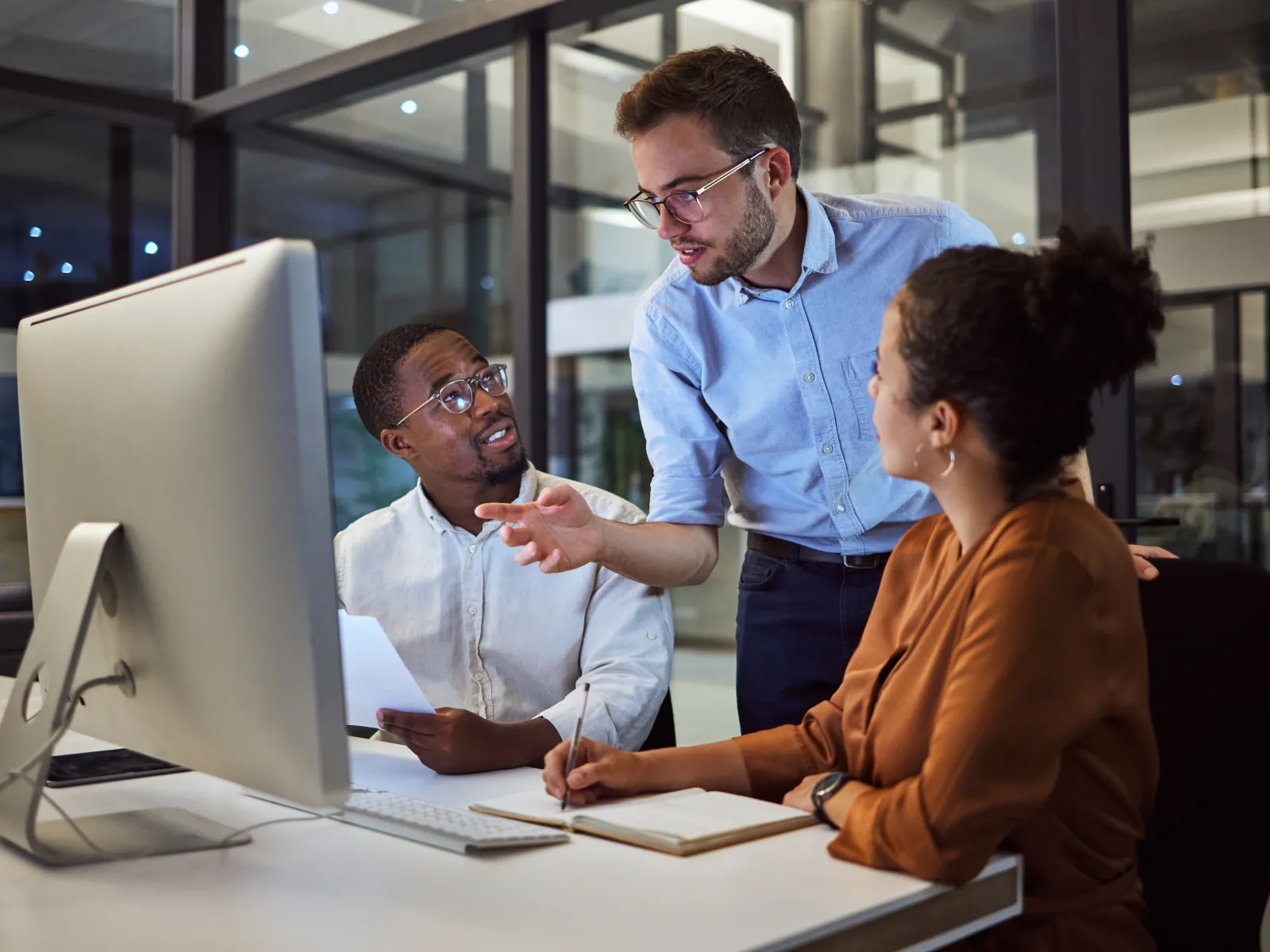Three colleagues collaborating in a modern office environment at night with a computer.